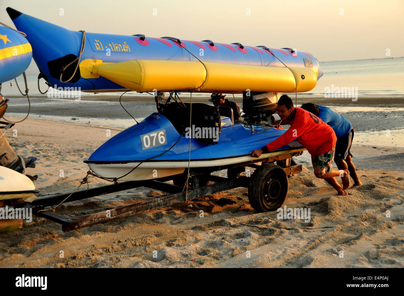 Bang Saen, Thaïlande : les travailleurs thaïlandais poussant un bateau lutte pour l'obtenir à travers le sable profond à la fin de la journée Banque D'Images