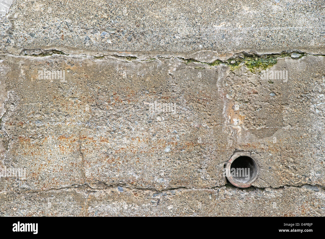 Un vieux mur de soutènement extérieur avec un tuyau d'écoulement en argile et des craquelures de surface avec des algues. Banque D'Images