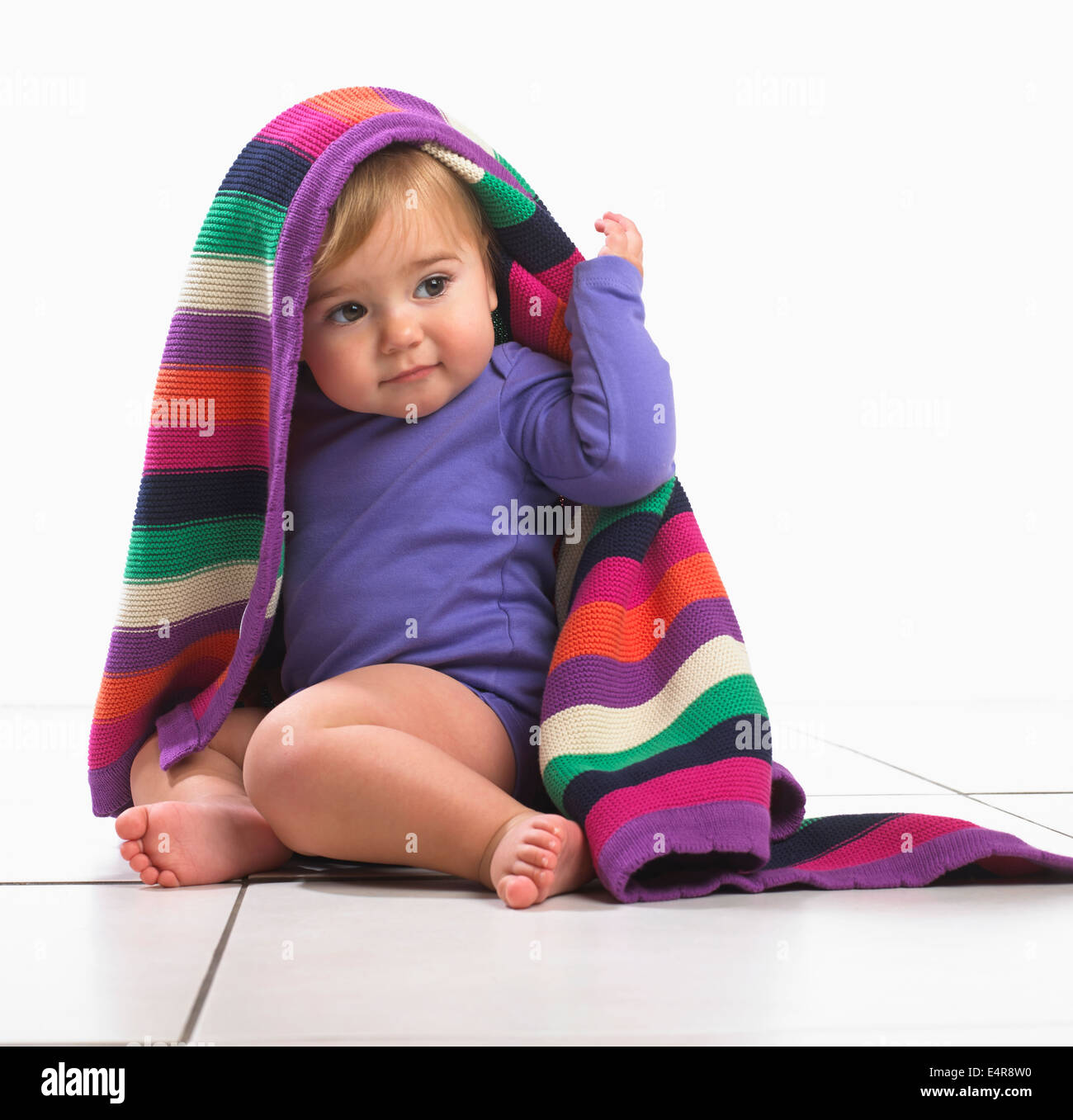 Bébé fille (12 mois) avec couverture à rayures colorées sur la tête. Banque D'Images