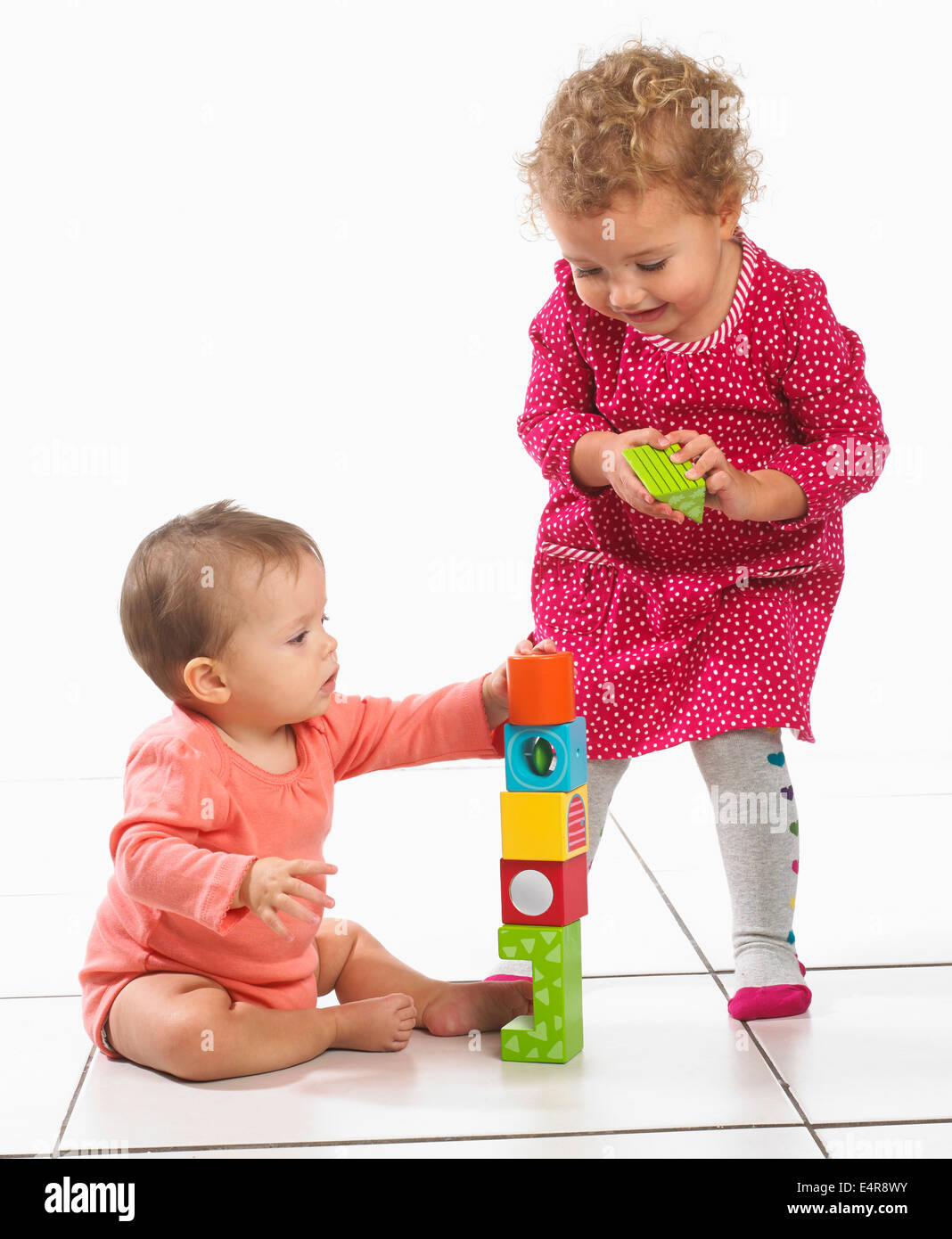 Bébé fille (8 mois) et d'enfant (2 ans) construire tour avec blocs colorés Banque D'Images