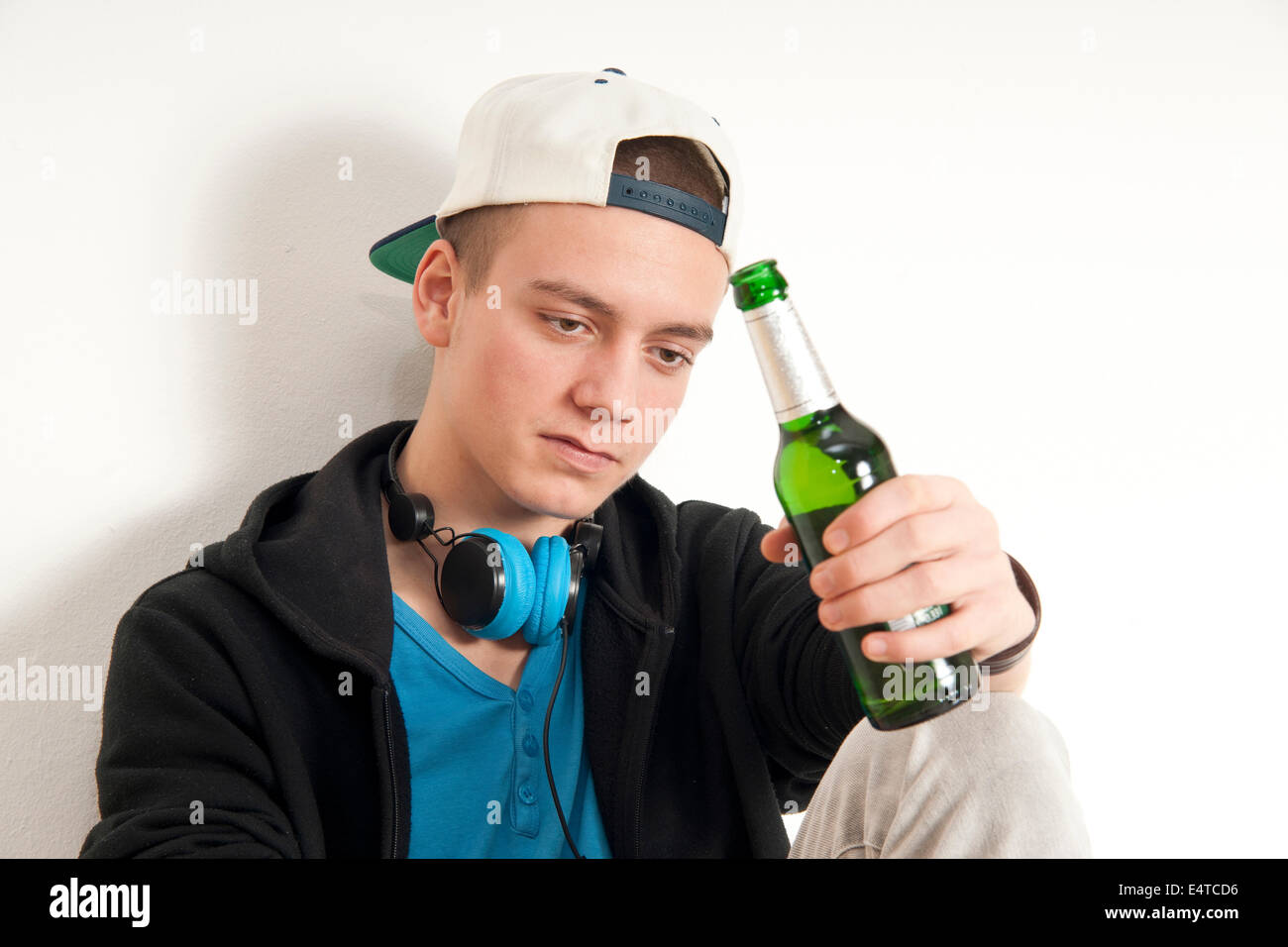 Teenage boy wearing hat avec des écouteurs autour du cou, tenant une bouteille de bière, studio shot on white background Banque D'Images