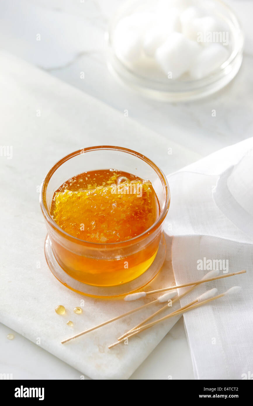 Pot de miel doré clair et un rayon à miel avec des tampons de coton et de boules de coton. High key image des produits de beauté Banque D'Images