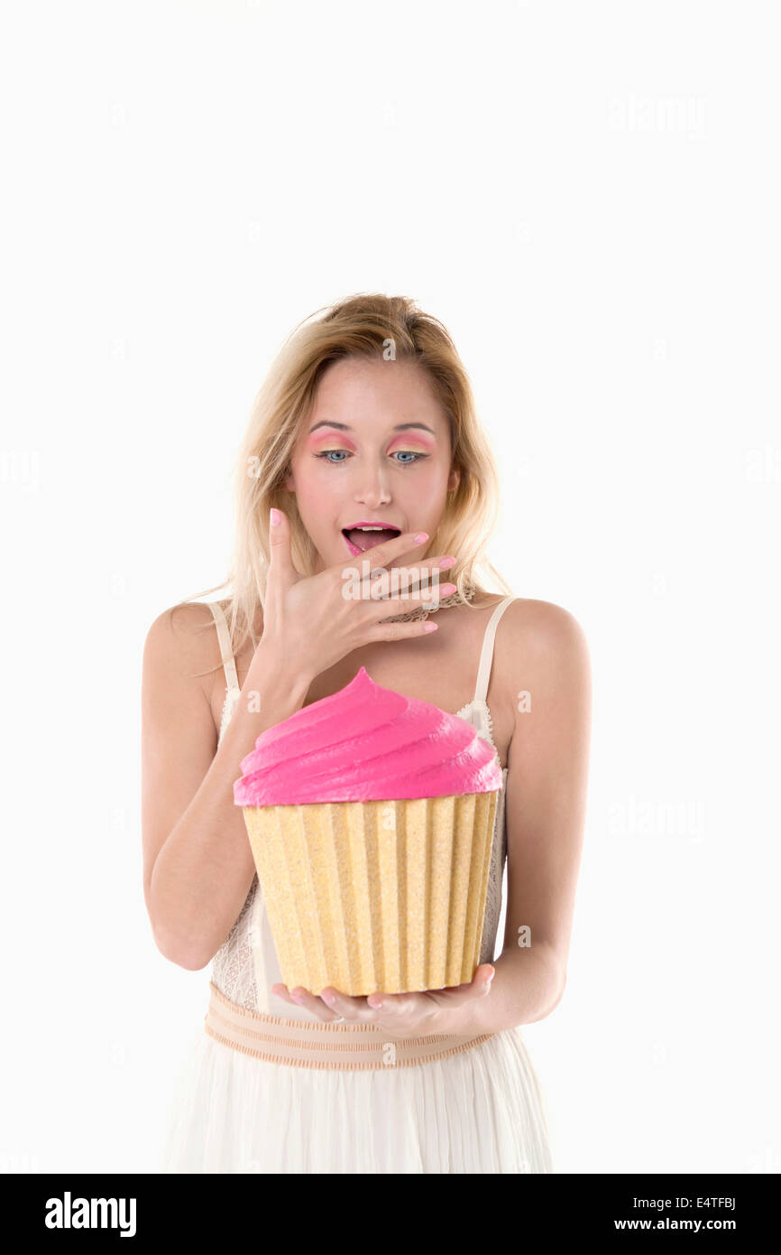 Portrait of young woman holding cupcake géant et à la surprise, studio shot on white background Banque D'Images