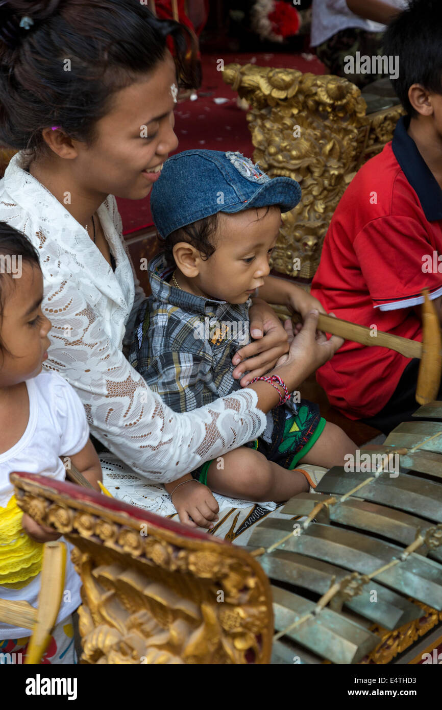 Bali, Indonésie. L'hindouisme balinais mère montrant comment l'enfant à frapper un xylophone avec son marteau en bois. Banque D'Images