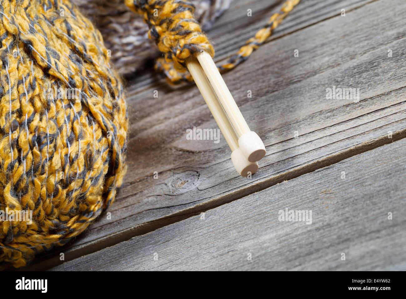 Vue rapprochée de l'angle des aiguilles à tricoter en bois, l'accent sur la partie inférieure, avec des boules de laine en arrière-plan sur bois rustique Banque D'Images