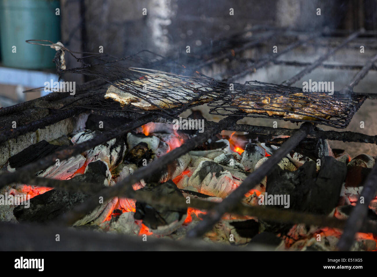 Bali, Indonésie. Griller le poisson sur un feu de charbon dans un petit stand de restauration rapide dans le marché aux poissons de Jimbaran. Banque D'Images