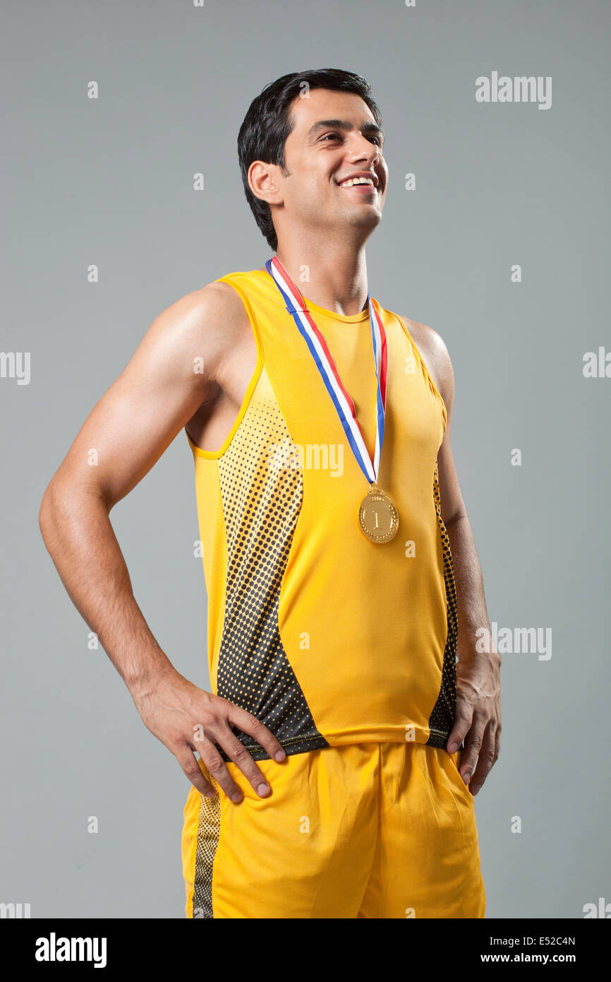 Heureux homme portant médaille d'or avec les mains sur la hanche contre l'arrière-plan gris Banque D'Images