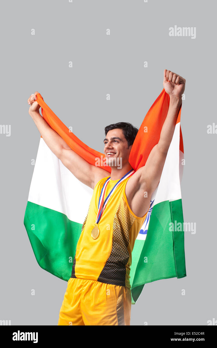 Médaillé d'hommes célébrant la victoire avec drapeau indien contre l'arrière-plan gris Banque D'Images