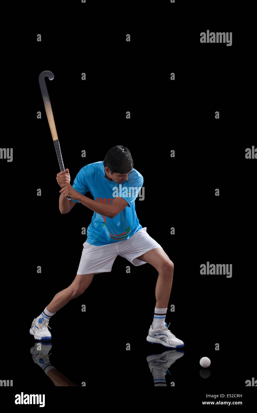 Jeune Indien hockey player sur le point de frapper une balle sur fond noir isolé Banque D'Images