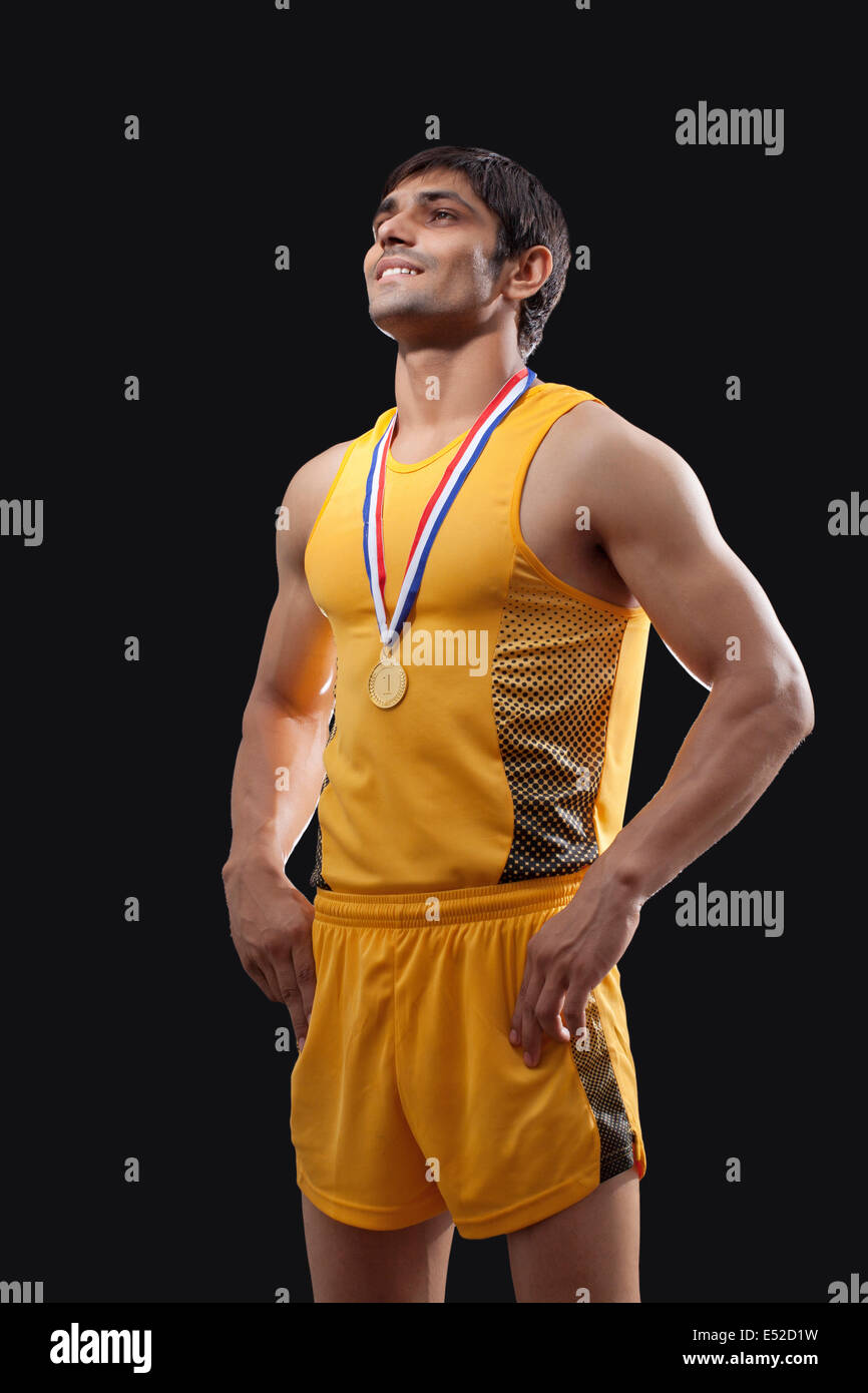 Heureux de la médaille d'or masculine debout avec les mains sur la taille sur fond noir Banque D'Images