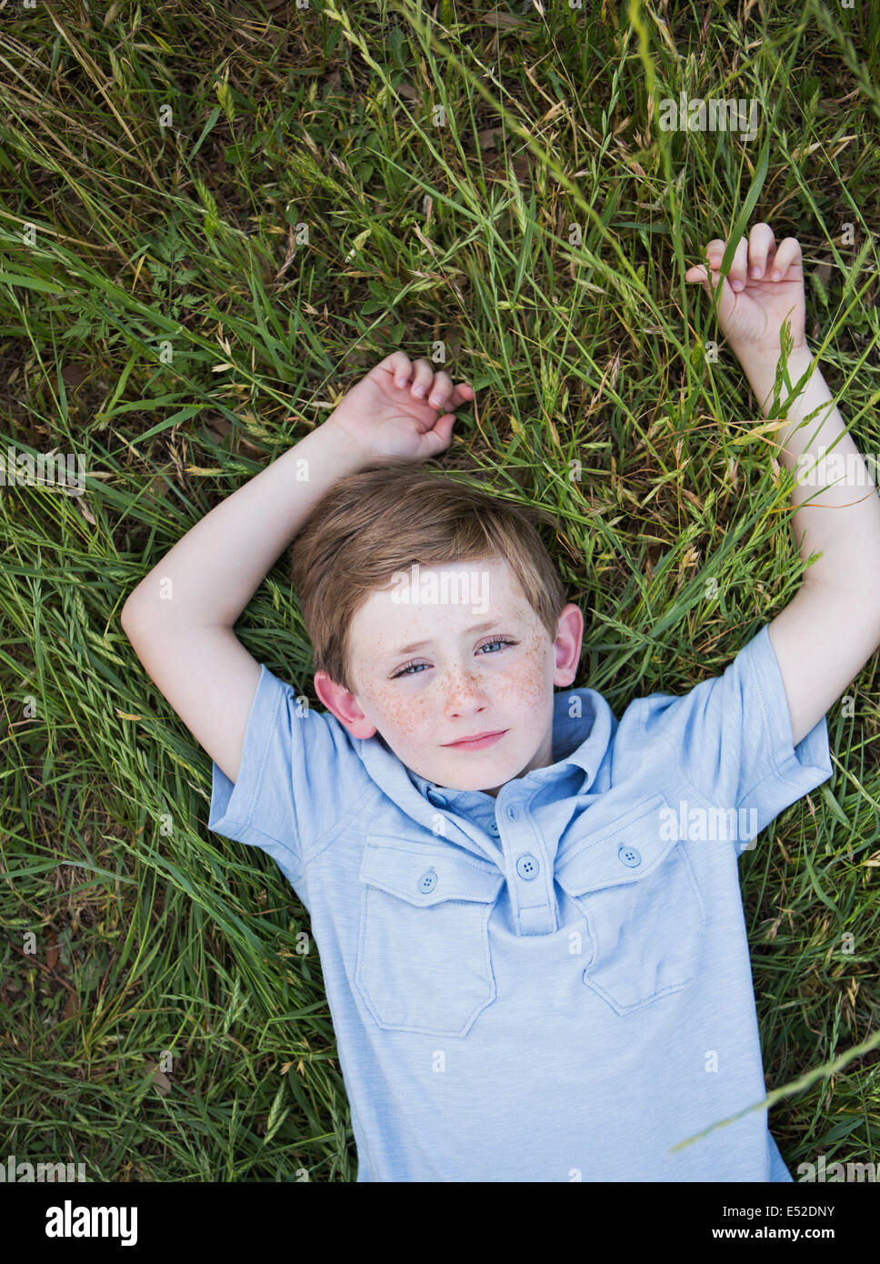 Un garçon dans une chemise bleue allongé sur le dos sur l'herbe. Banque D'Images