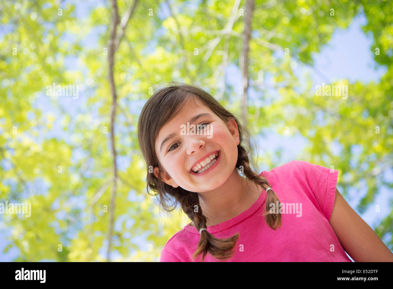 Une jeune fille aux tresses, vêtu d'un haut rose sous un dais d'arbres. Banque D'Images