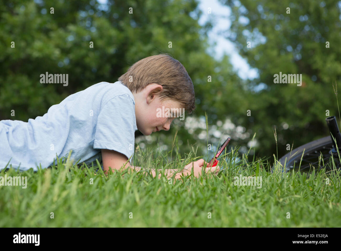 Un jeune garçon couché dans l'herbe de la lecture d'un jeu électronique de poche. Banque D'Images