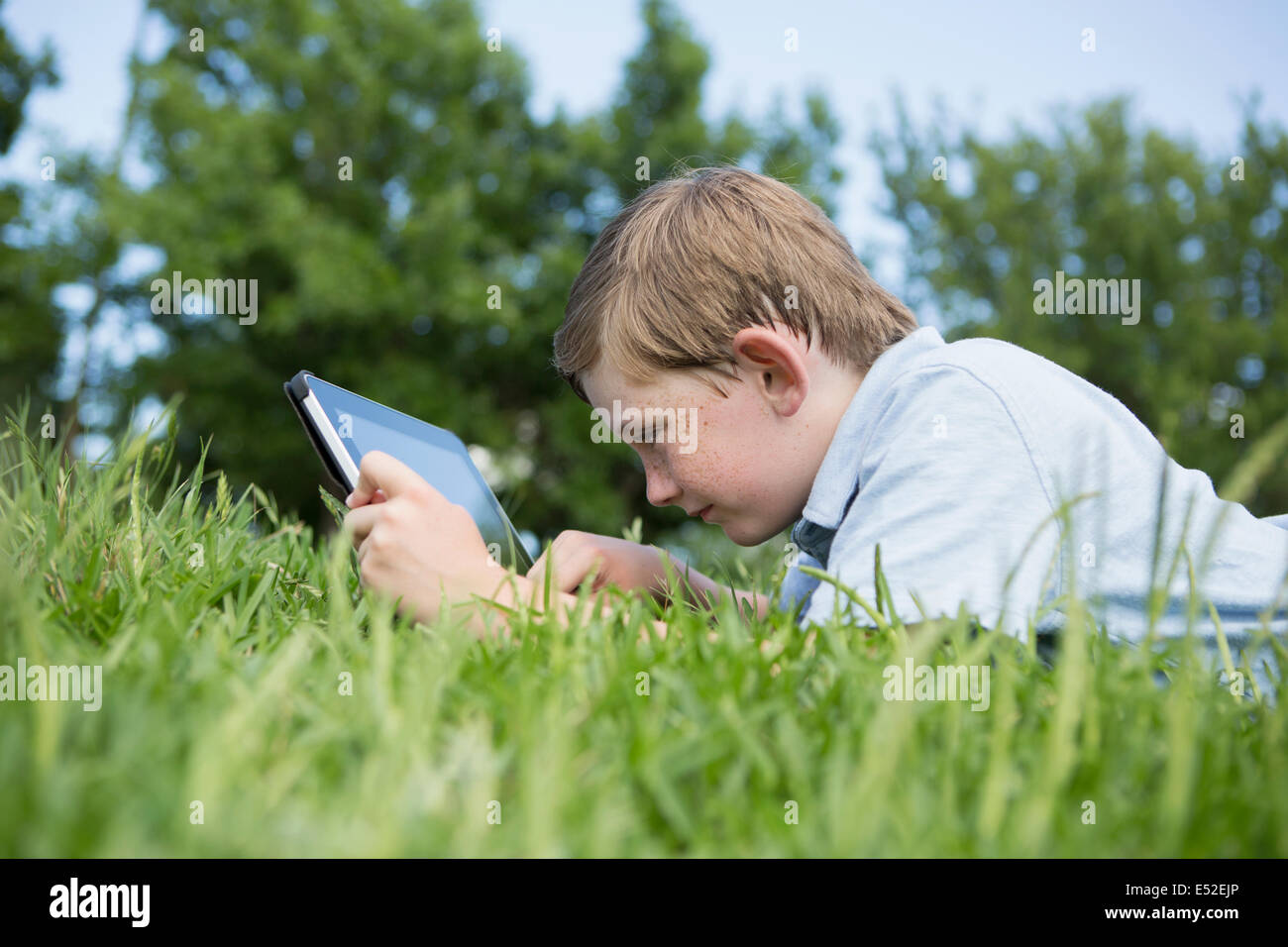 Un jeune garçon couché dans l'herbe, à l'aide d'une tablette numérique. Banque D'Images