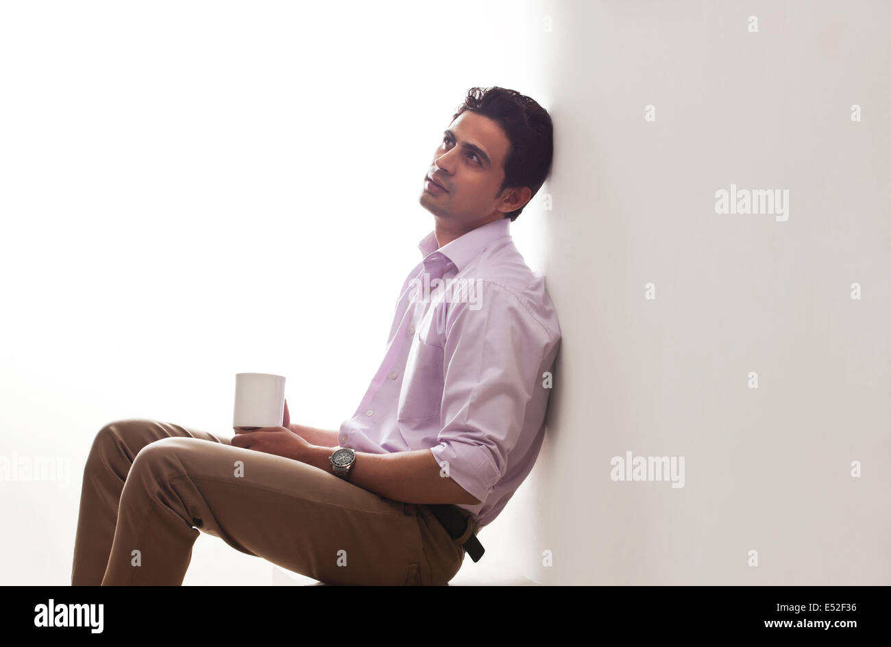 Homme tenant une tasse de thé leaning against wall Banque D'Images
