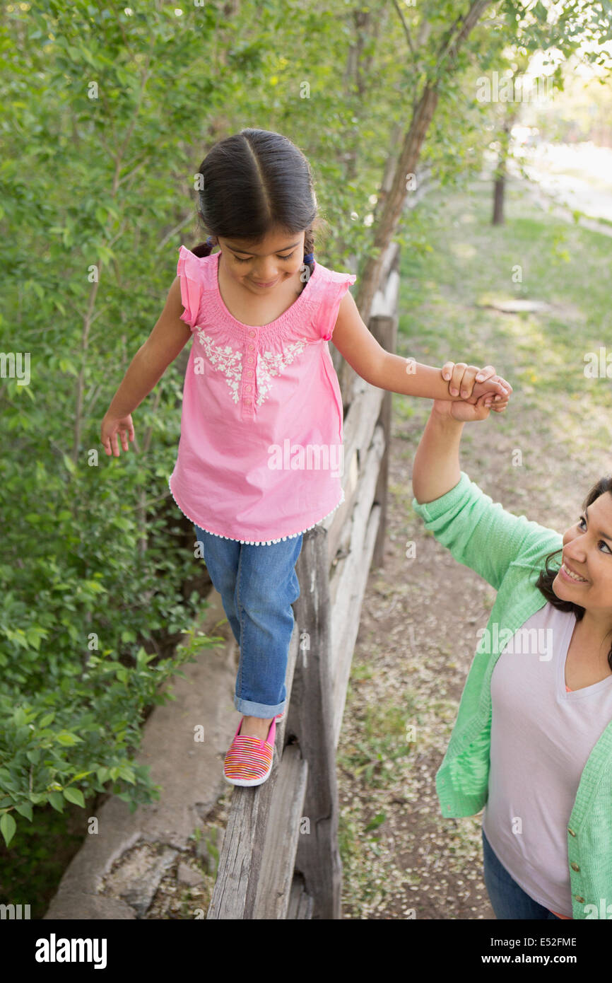 Une jeune fille dans un chandail rose et un jean, marcher le long d'une clôture tenant la main de sa mère. Banque D'Images