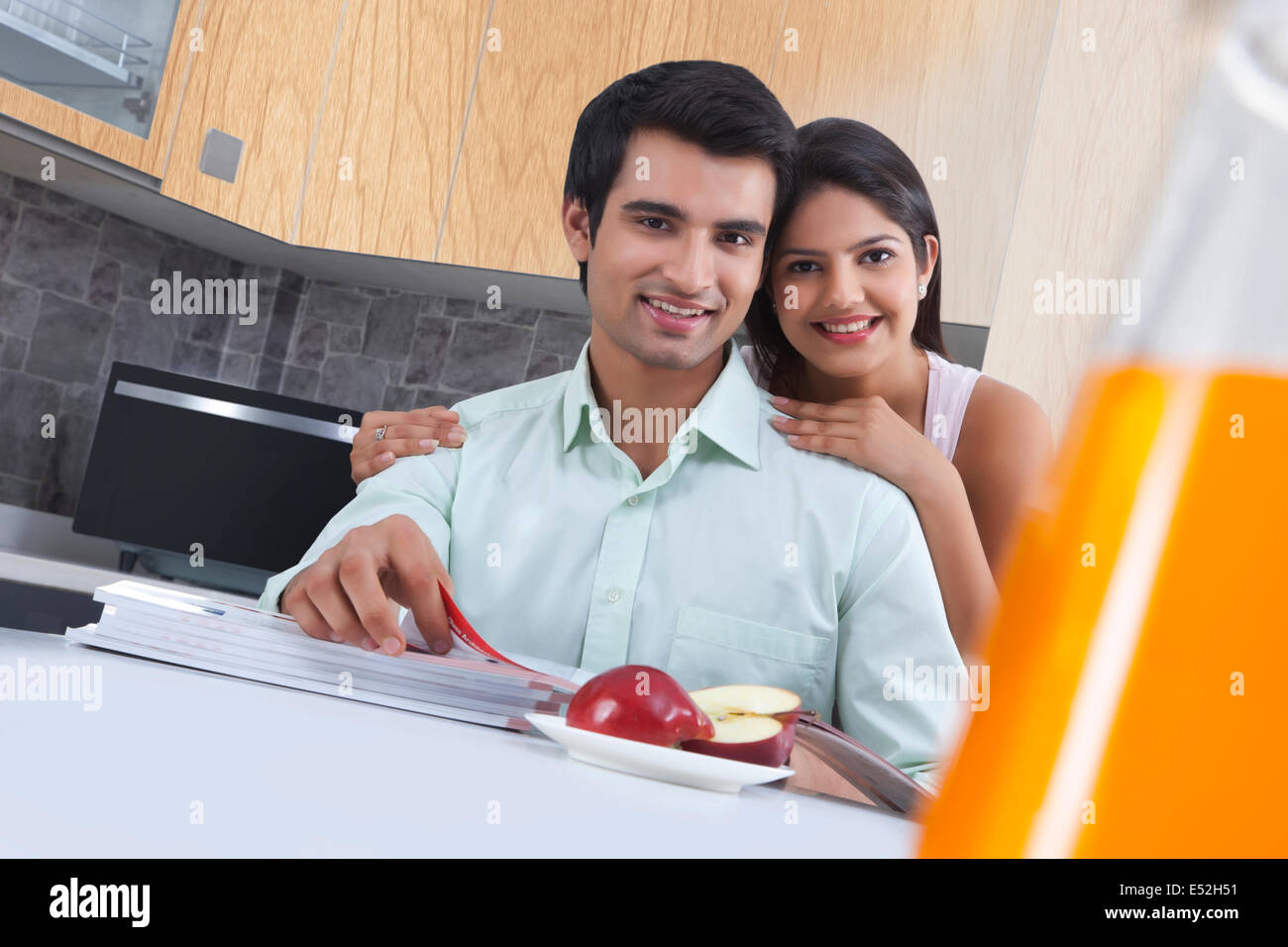 Portrait of smiling couple avec des catalogues et Apple à l'île de cuisine Banque D'Images