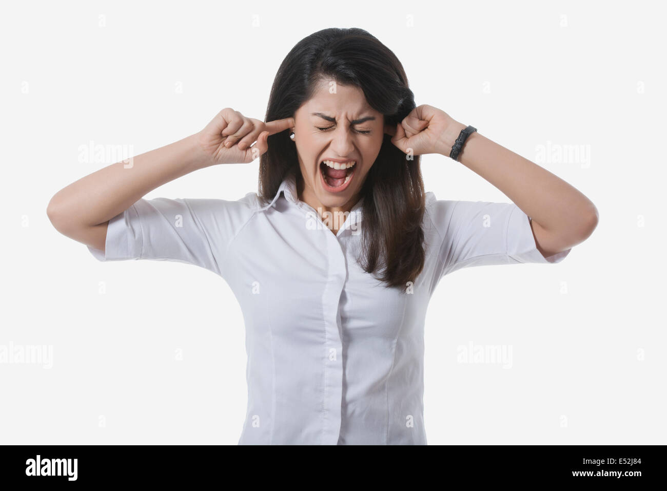 Frustrated businesswoman avec les doigts dans les oreilles de crier contre fond blanc Banque D'Images