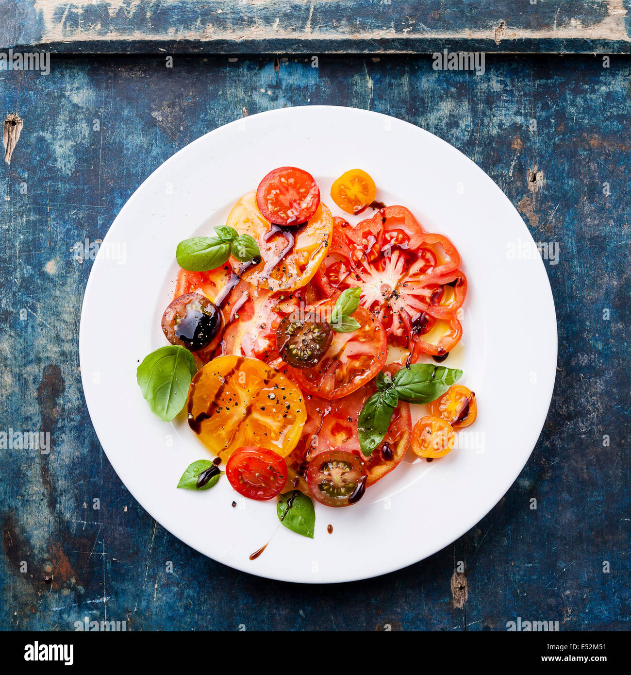 Frais salade de tomates mûres colorés avec de l'huile d'olive et de vinaigre balsamique sur fond de bois bleu Banque D'Images