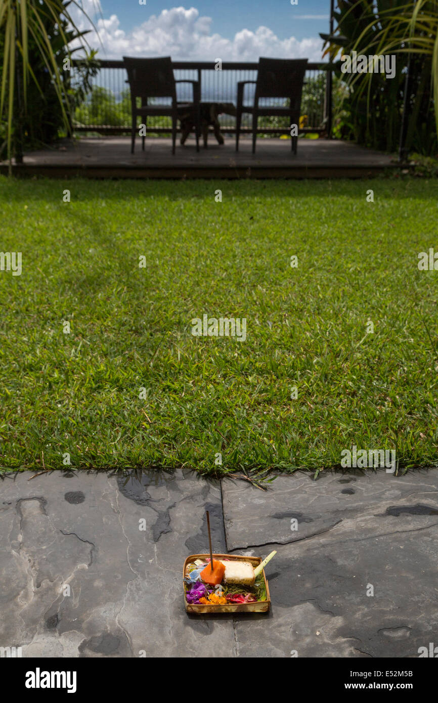 Bali, Indonésie. Une offrande (Canang) de pétales de fleurs, la papaye, et le pain se trouve sur le bord d'un petit jardin d'une maison locale. Banque D'Images