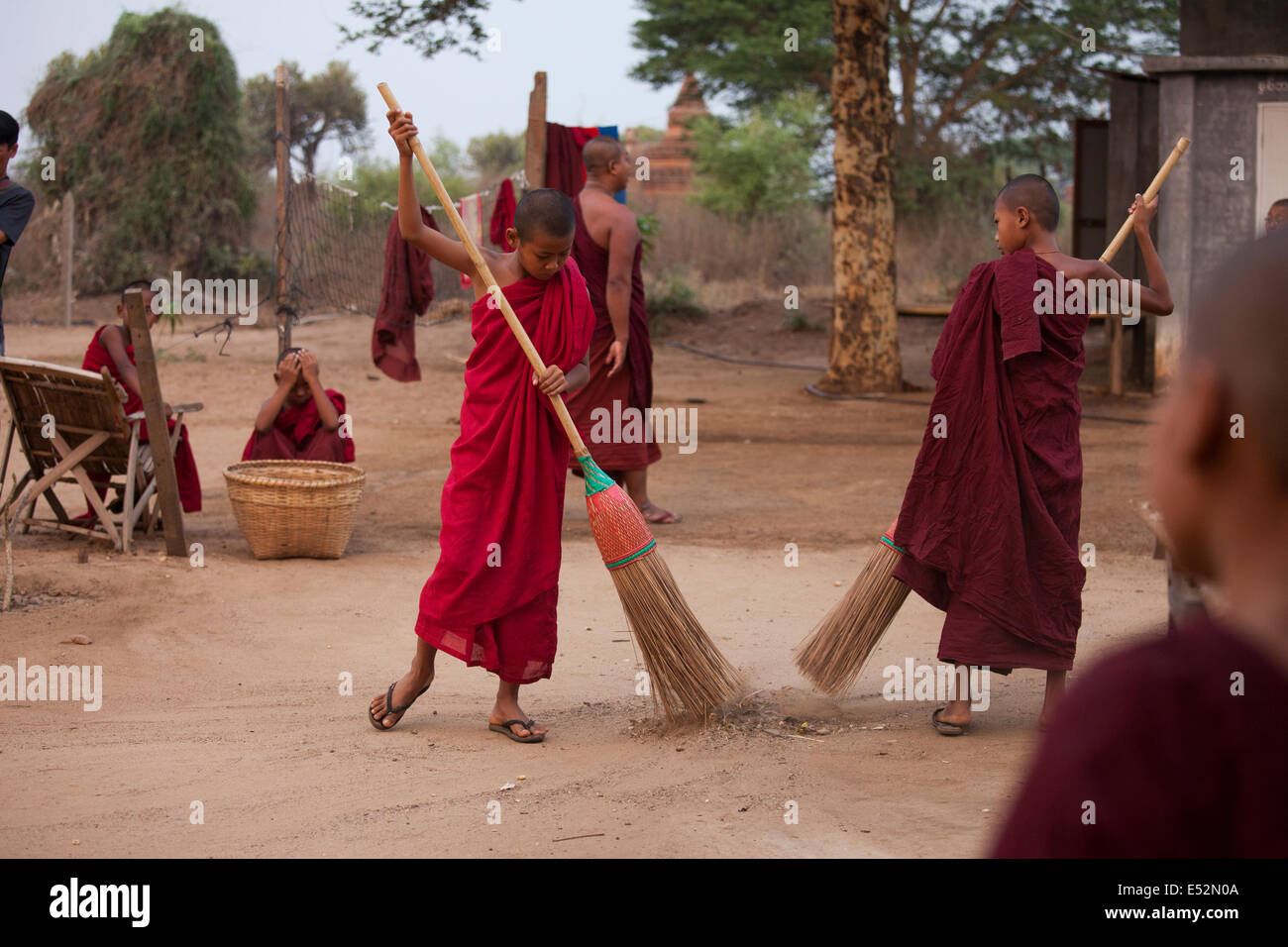 Jeunes moines aident à nettoyer les motifs de leur petit monastère de Bagan. Après que les motifs sont balayées avec manches, la région est arrosée. Banque D'Images