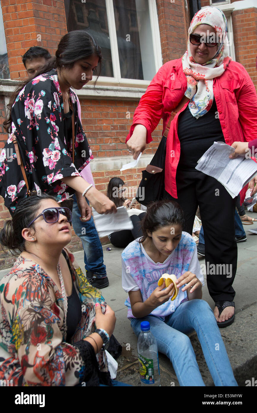 Londres, Royaume-Uni. Samedi 19 juillet 2014. Pro-Palestinian manifestants dans leurs dizaines de milliers de mars à central London à l'ambassade d'Israël en protestation contre l'offensive militaire à Gaza par Israël. Jeune fille qui est le jeûne de Ramadan, passe dehors et est relancé avec de l'eau et une banane par sa famille qu'ils papier vague pour refroidir la en bas. Crédit : Michael Kemp/Alamy Live News Banque D'Images