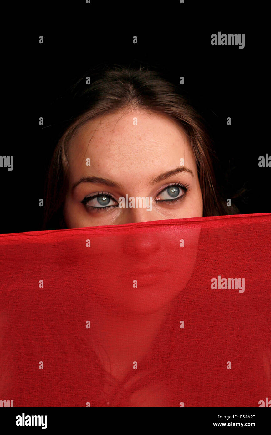 Jeune femme aux yeux bleus couvrant son visage avec un voile rouge Banque D'Images