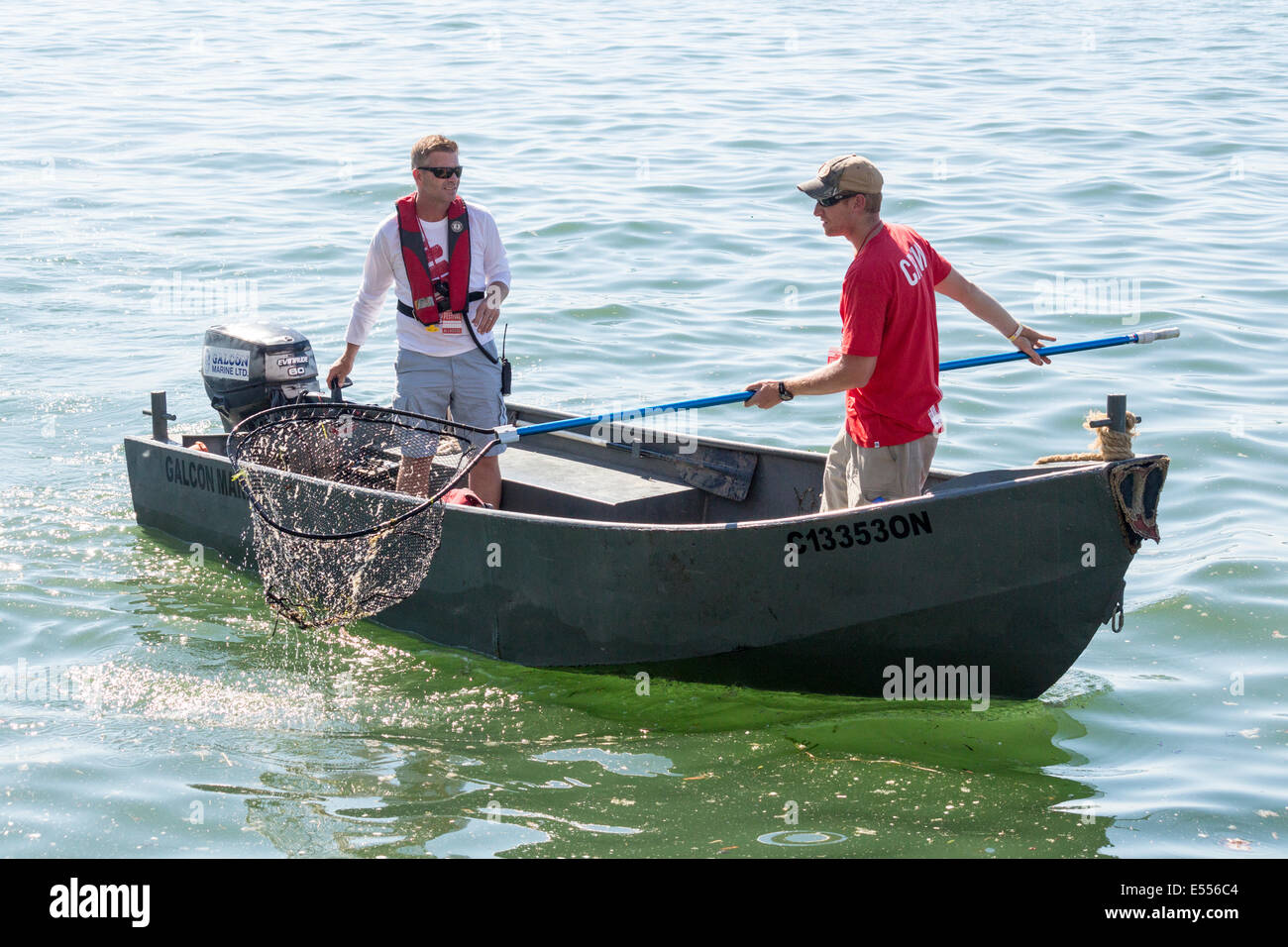 Deux jeunes ment dans les petites embarcations à l'aide de net pour nettoyer les débris hors de l'eau. Banque D'Images