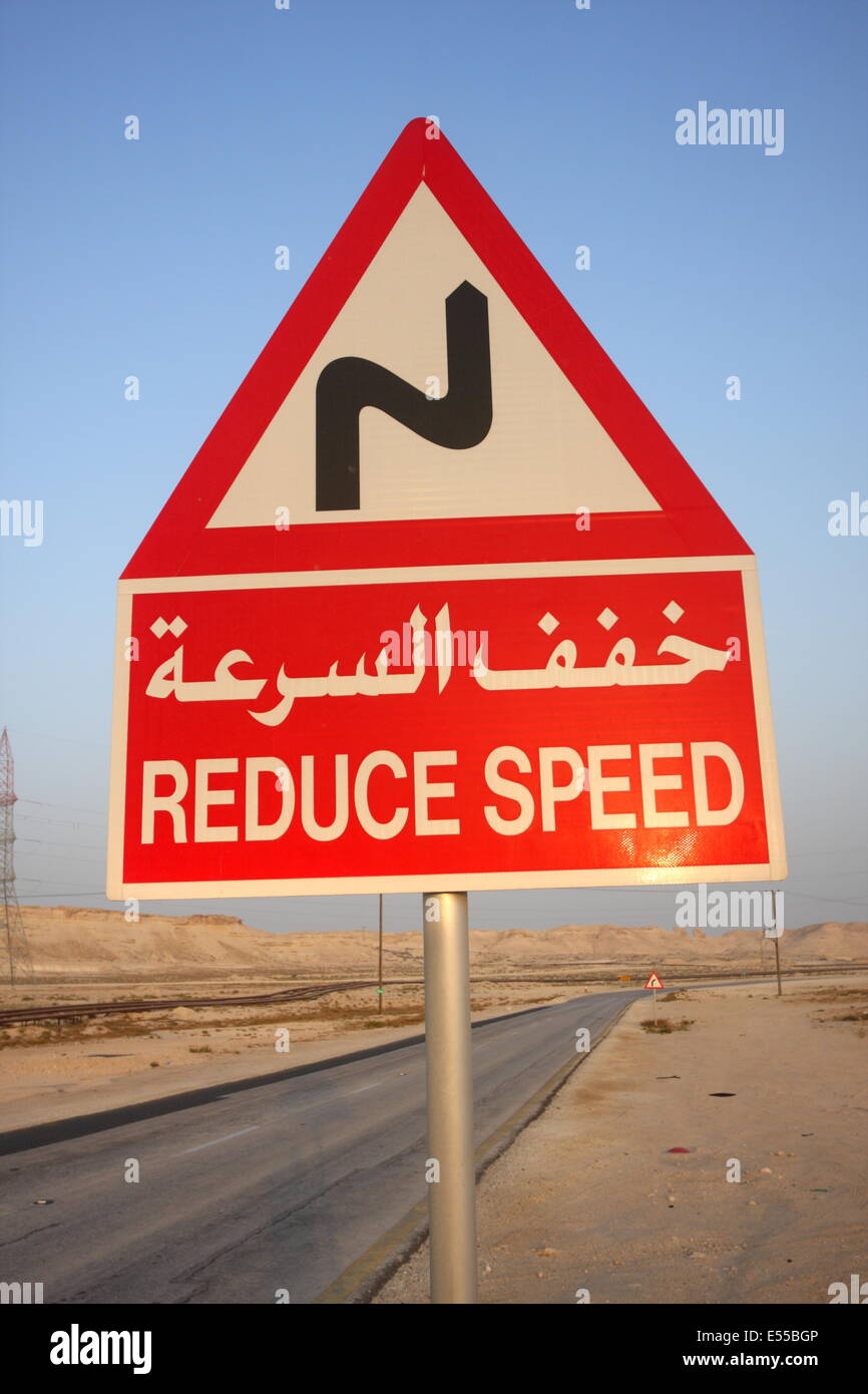 Une signalisation routière en arabe et français raconter les automobilistes à réduire leur vitesse en raison d'un virage de la route, dans le Royaume de Bahreïn Banque D'Images