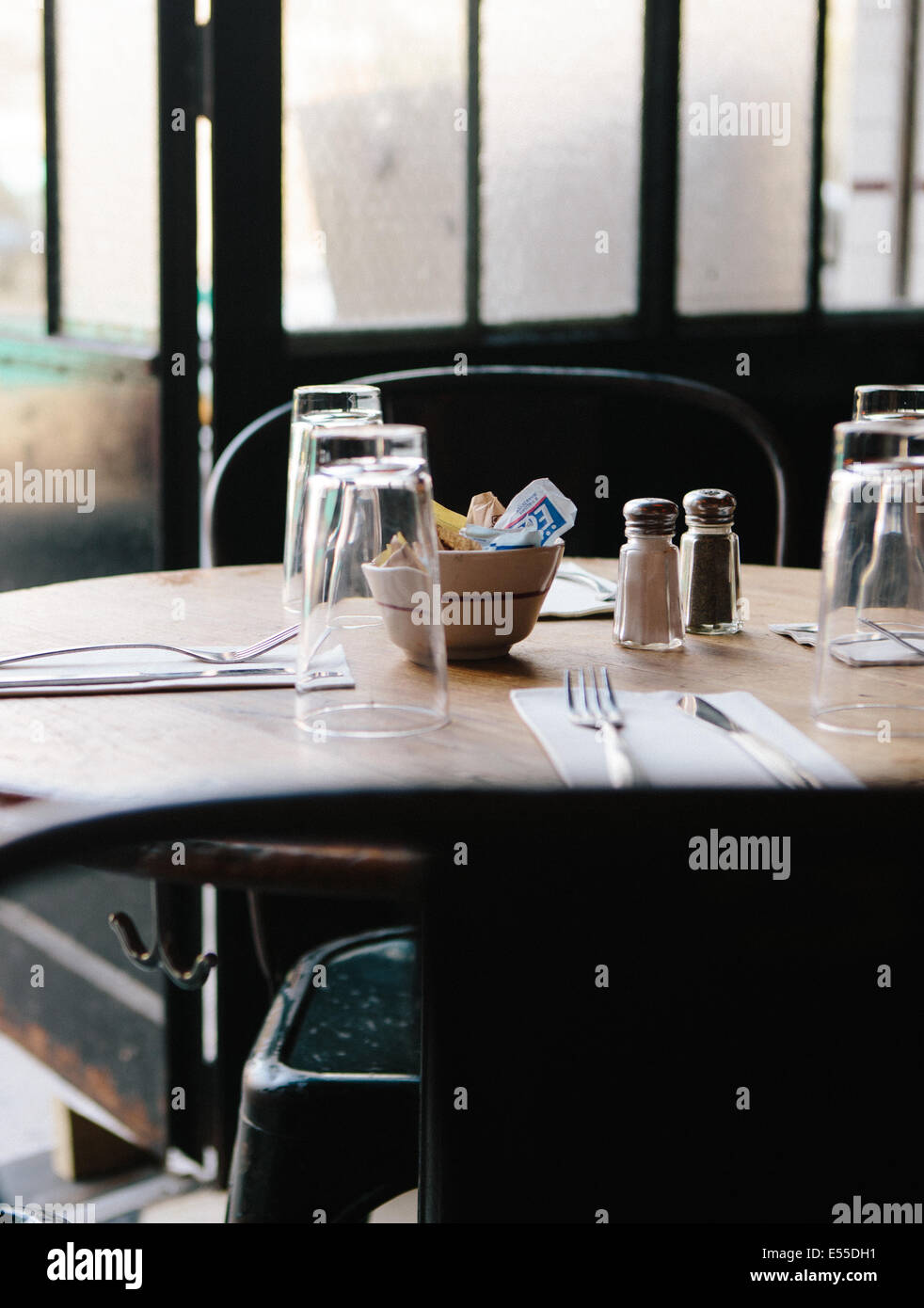 Detail shot de table avec des verres, salières et poivrières, et des serviettes en papier contre une porte en verre dépoli. Banque D'Images