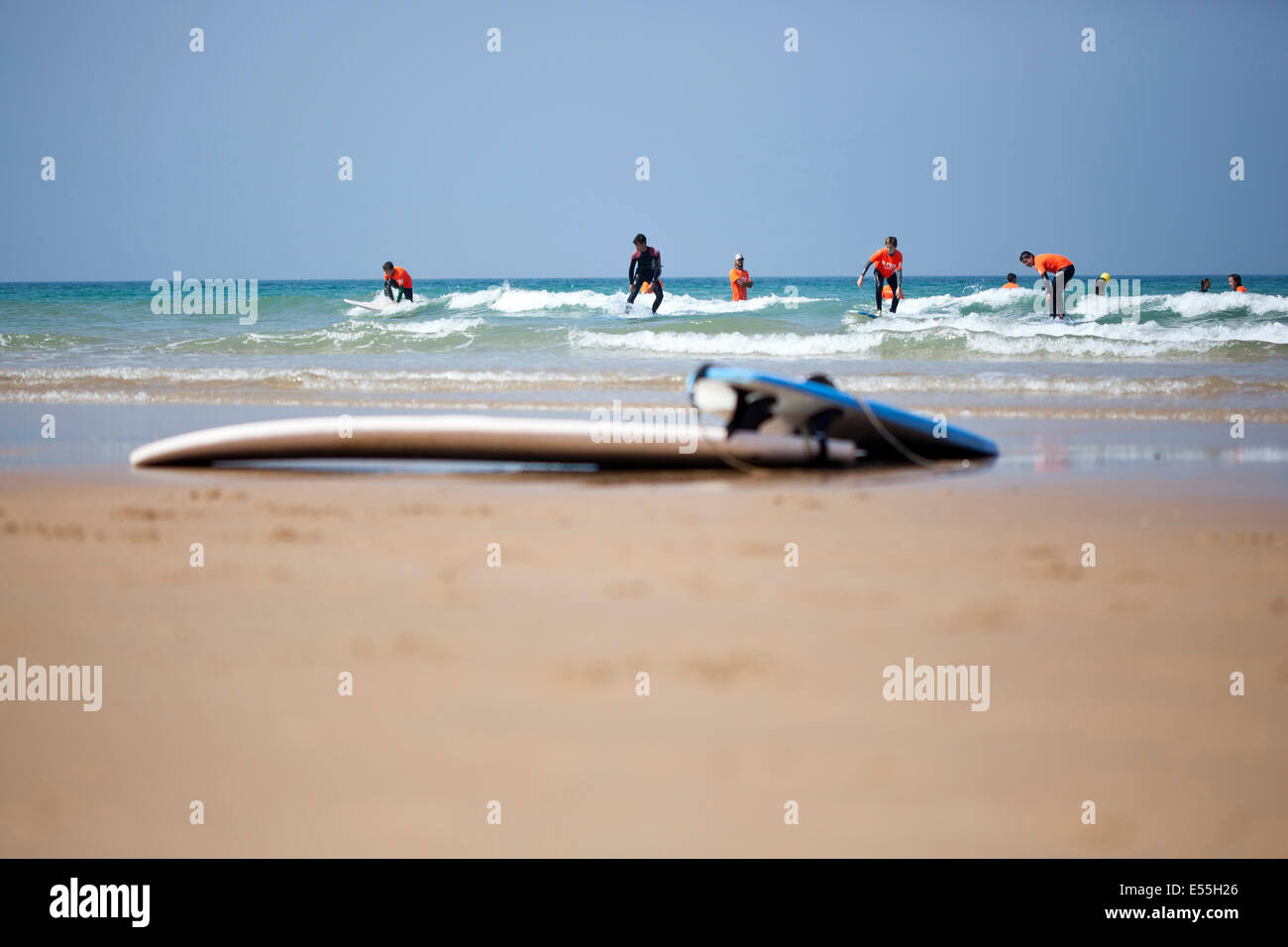 Groupe de personnes ayant des leçons de surf entre les vagues sur une plage de sable fin de l'Espagne et des planches en premier plan ciel bleu en arrière-plan Banque D'Images