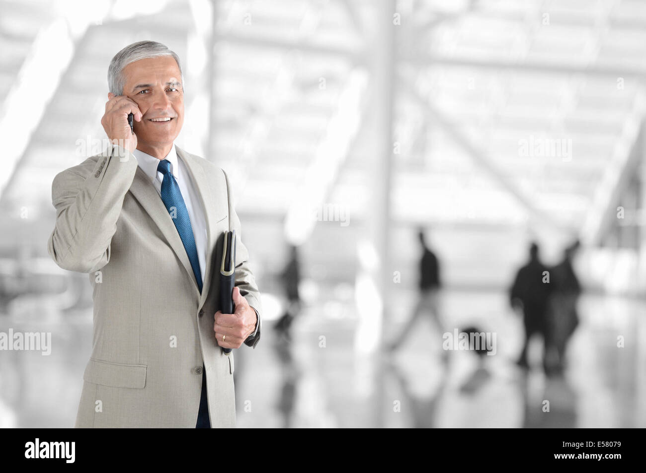 Un homme d'âge mûr sur son téléphone cellulaire dans un terminal de l'aéroport. L'arrière-plan est flou avec méconnaissable. Banque D'Images