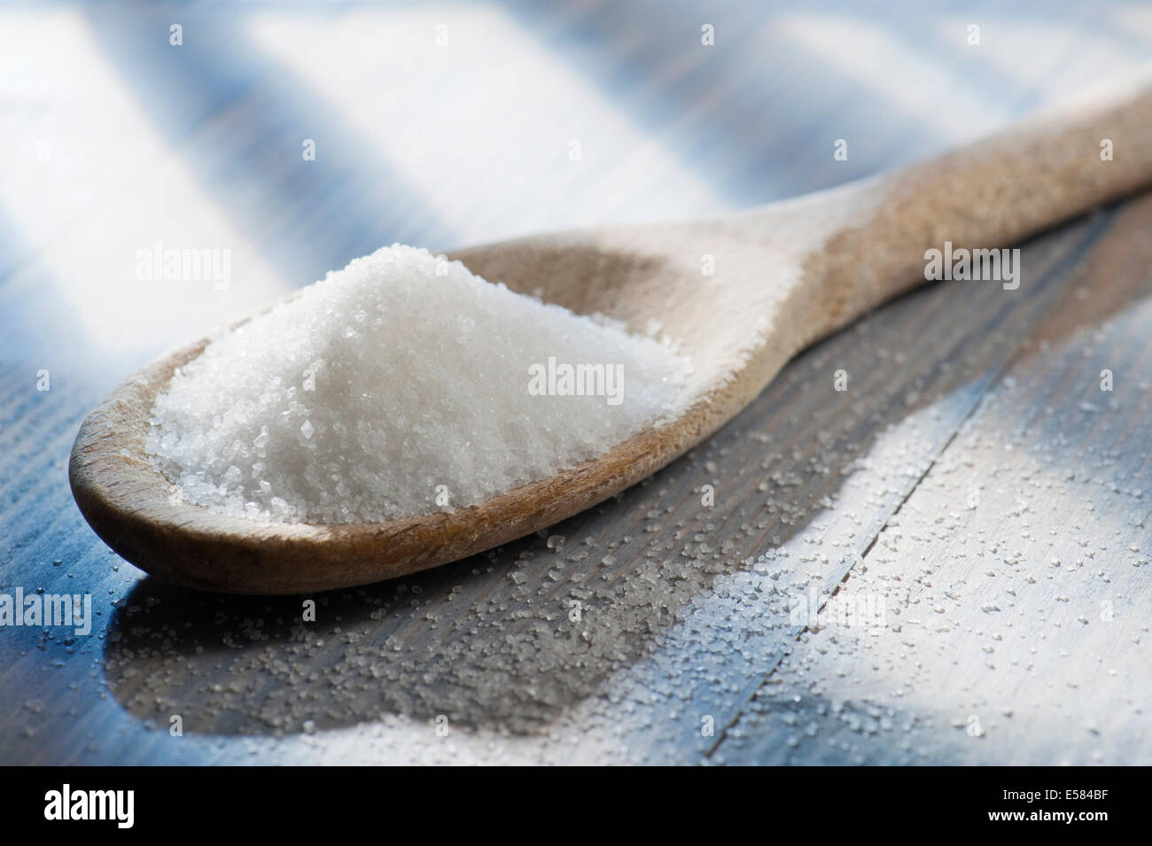 Sucre blanc en cuillère en bois sur la table en bois éclairé par le soleil Banque D'Images