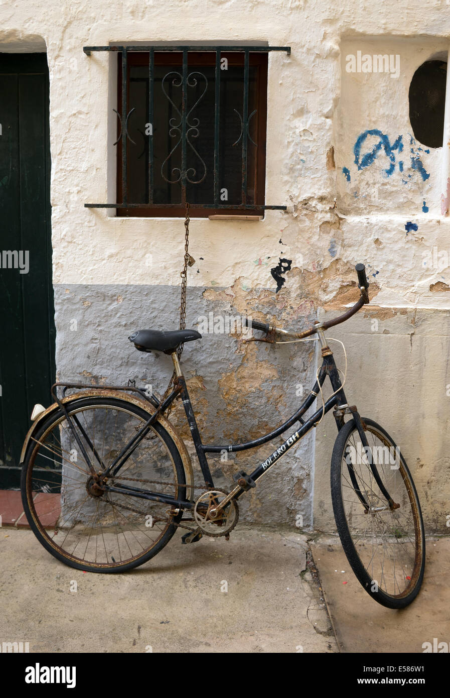 Vieux Vélo enchaîné à un cadre de fenêtre contre un mur dans une rue espagnole : Ciutadella, Menorca, Espagne. Banque D'Images