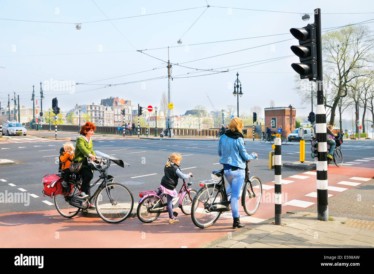 Les femmes et les enfants sur des vélos en attente à un franchissement routier, Amsterdam, Pays-Bas Banque D'Images