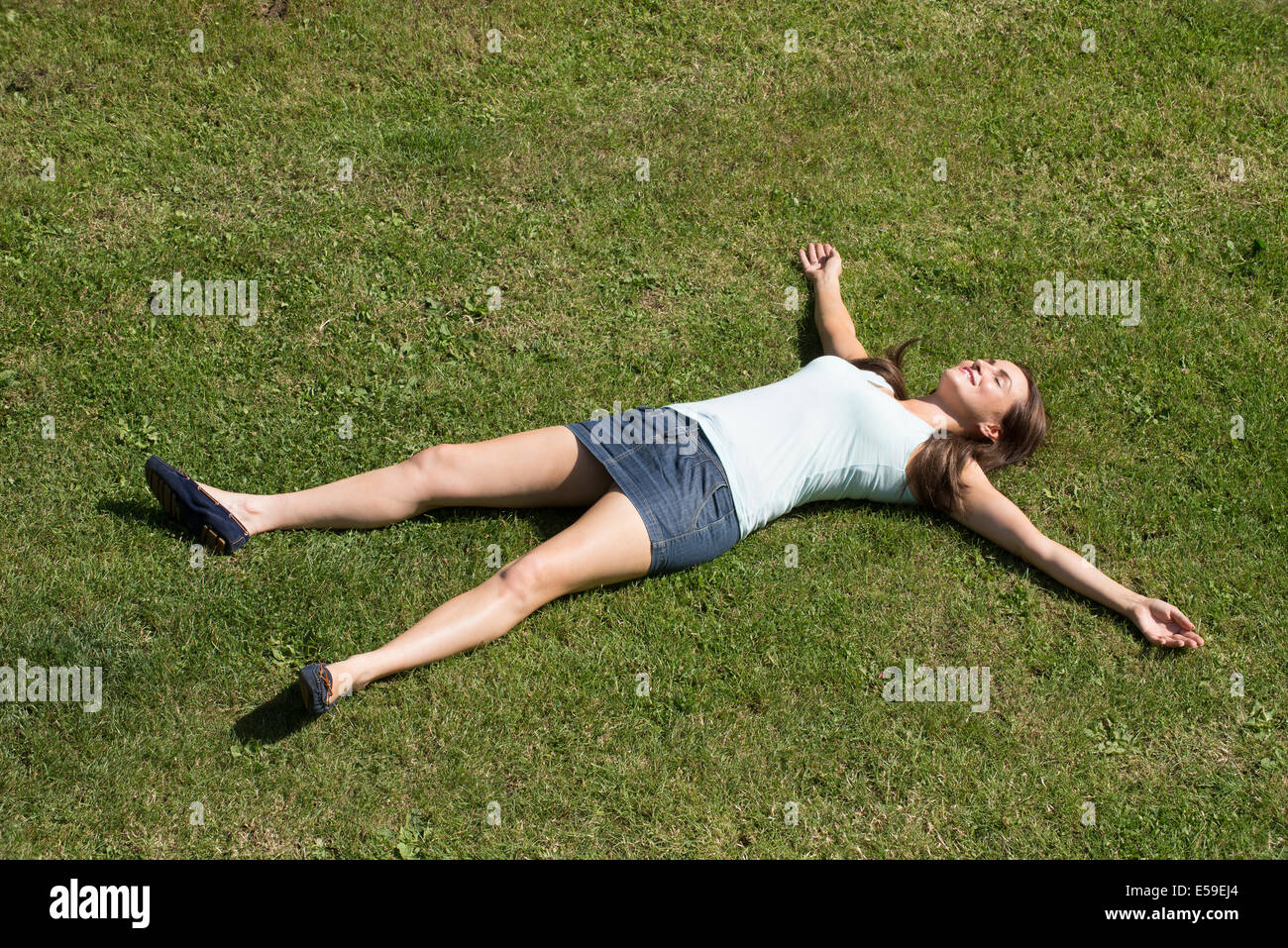 Jeune femme portant une mini jupe portant sur l'herbe avec les bras et les jambes tendus Banque D'Images