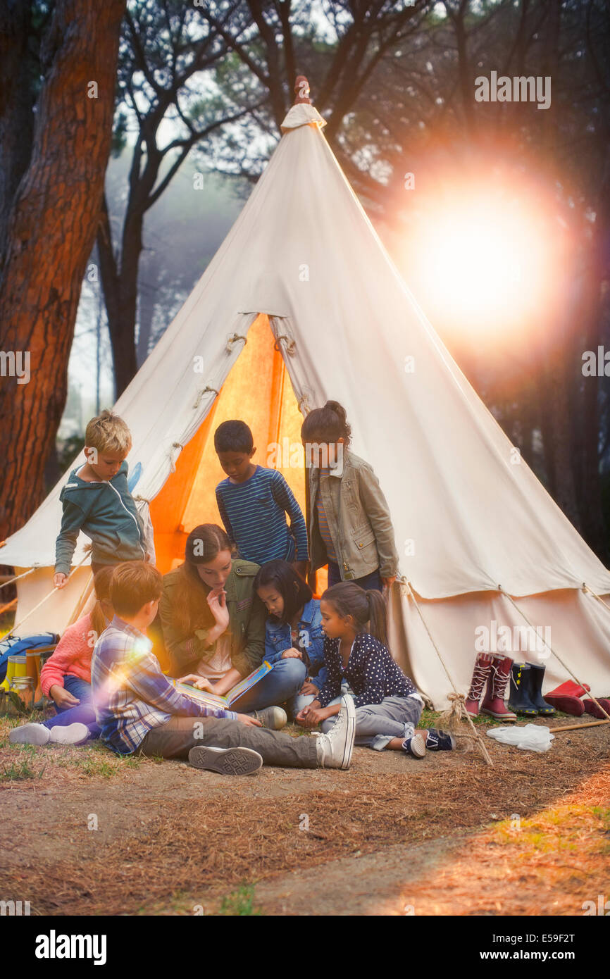 Les élèves et l'enseignant la lecture au tipi de camping Banque D'Images