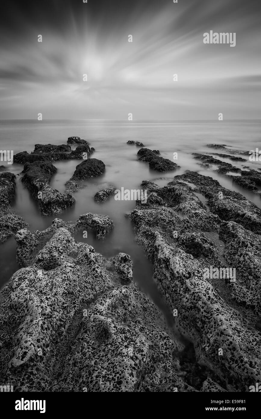 Paysage en noir et blanc face à la mer avec la côte rocheuse et magnifique coucher de soleil ciel Banque D'Images