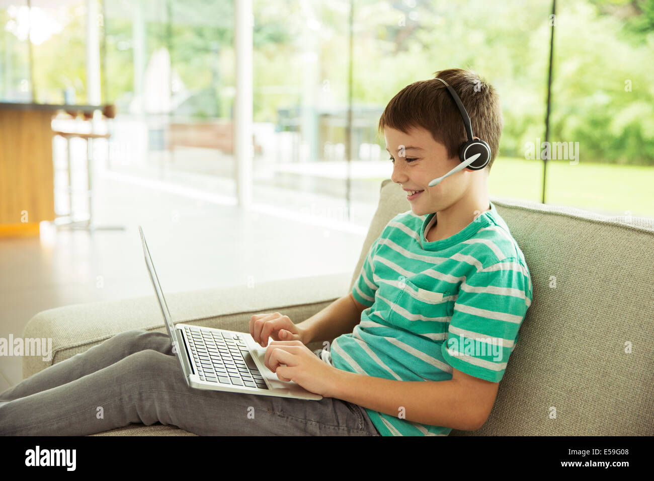 Boy wearing headset and using laptop on sofa Banque D'Images