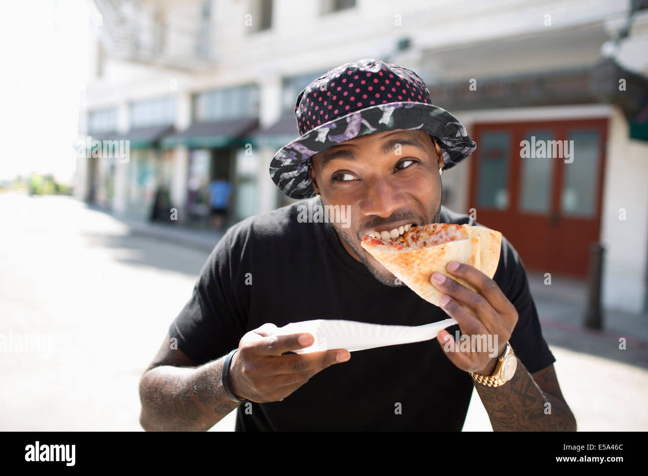 African American man eating pizza on city street Banque D'Images