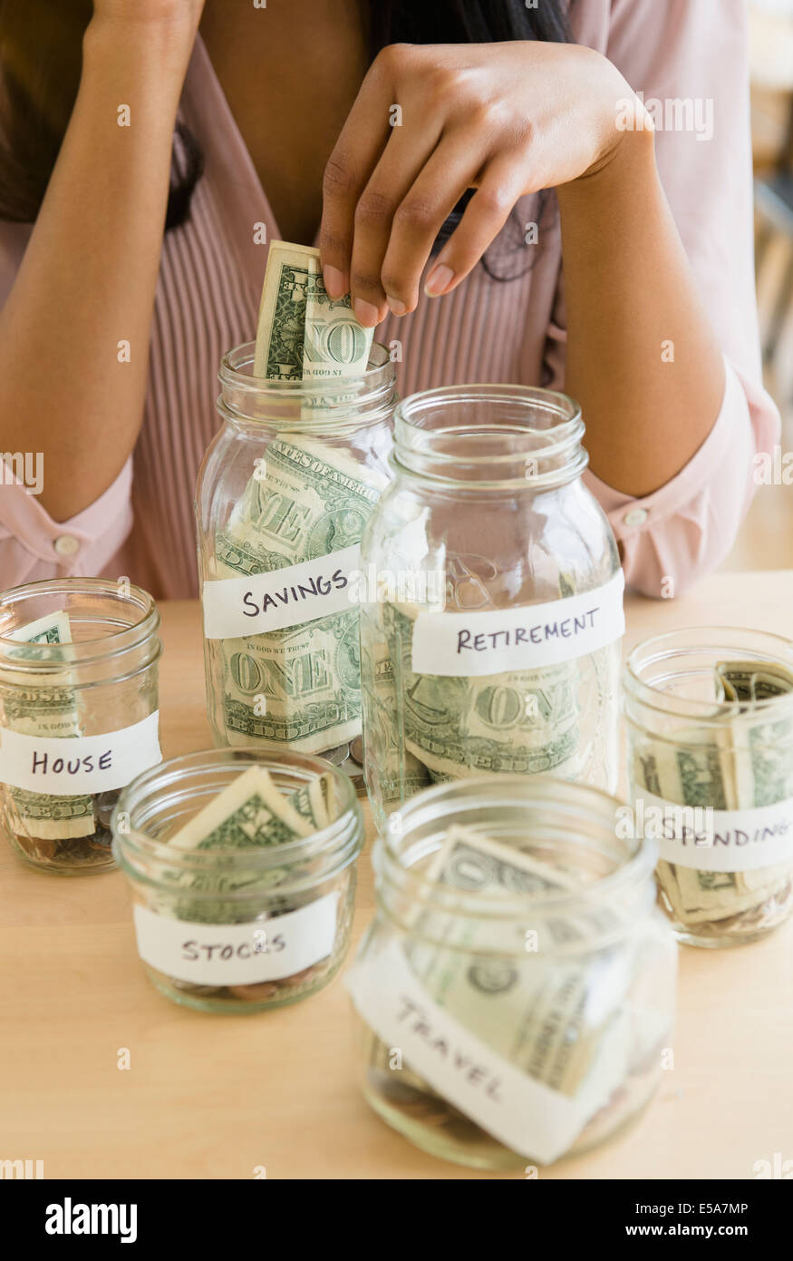 Mixed Race woman putting money in savings jars Banque D'Images