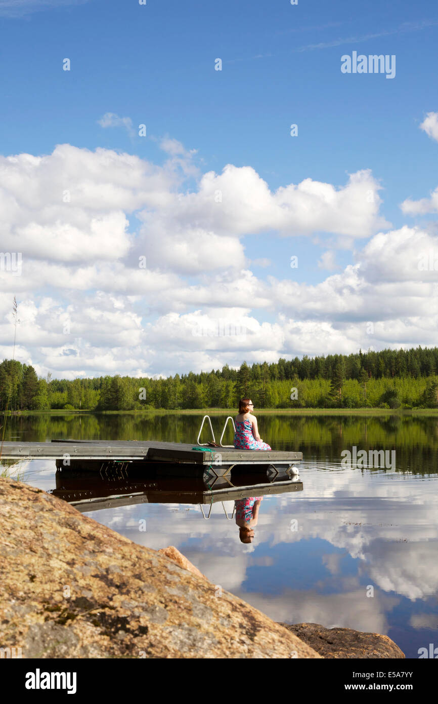 Le lac en été en Finlande avec une femme assise sur la jetée Banque D'Images