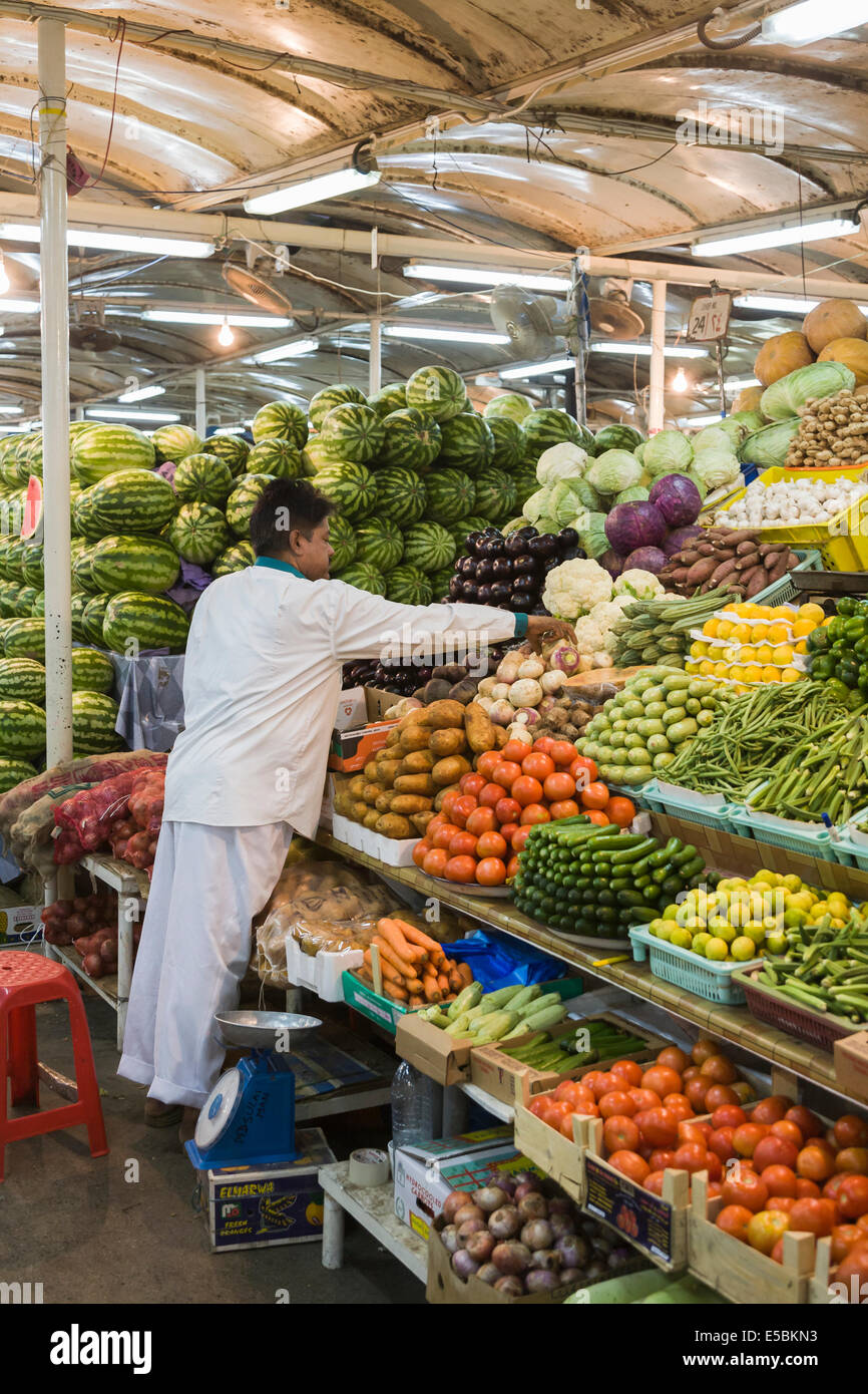 Vie : mâle locale exposant organise produire sur un étal de fruits et légumes colorés de vente au marché aux poissons, souk de Deira, Dubaï Banque D'Images