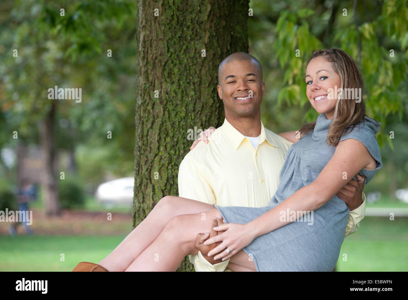 Une belle, heureuse et jeune couple interracial posant à côté d'un arbre sur une journée ensoleillée. Banque D'Images