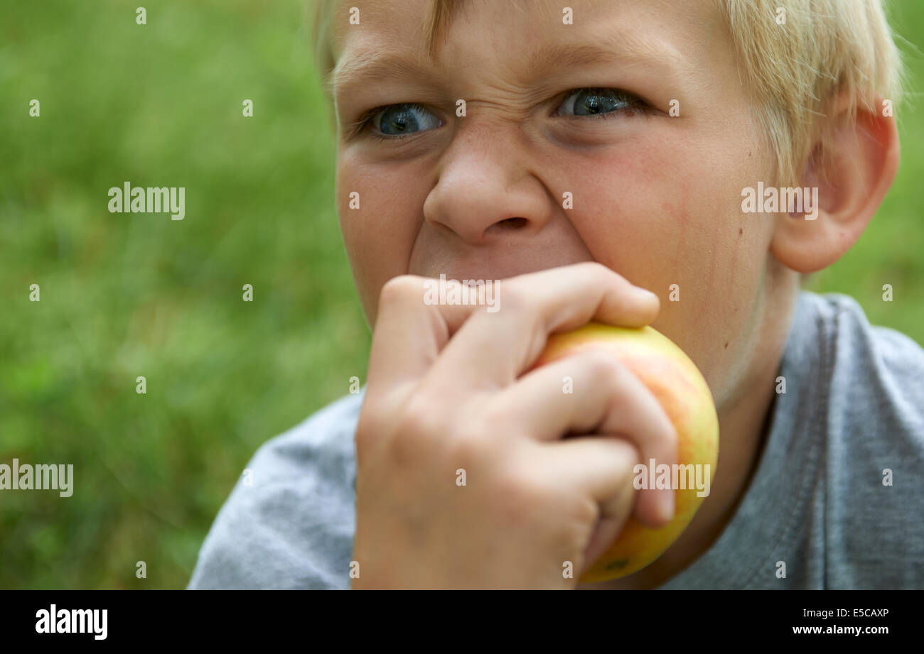 Portrait de l'enfant garçon blond Yeux bleu Eating Apple à l'extérieur, grin Banque D'Images