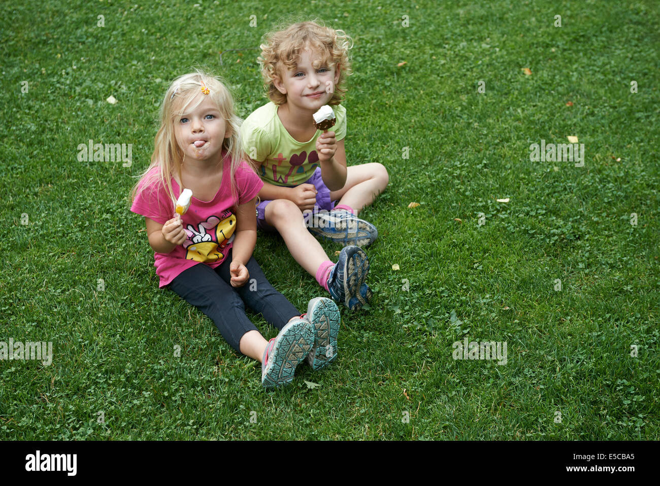 Enfants blondes eating ice cream cones assis sur la pelouse, l'heure d'été Banque D'Images