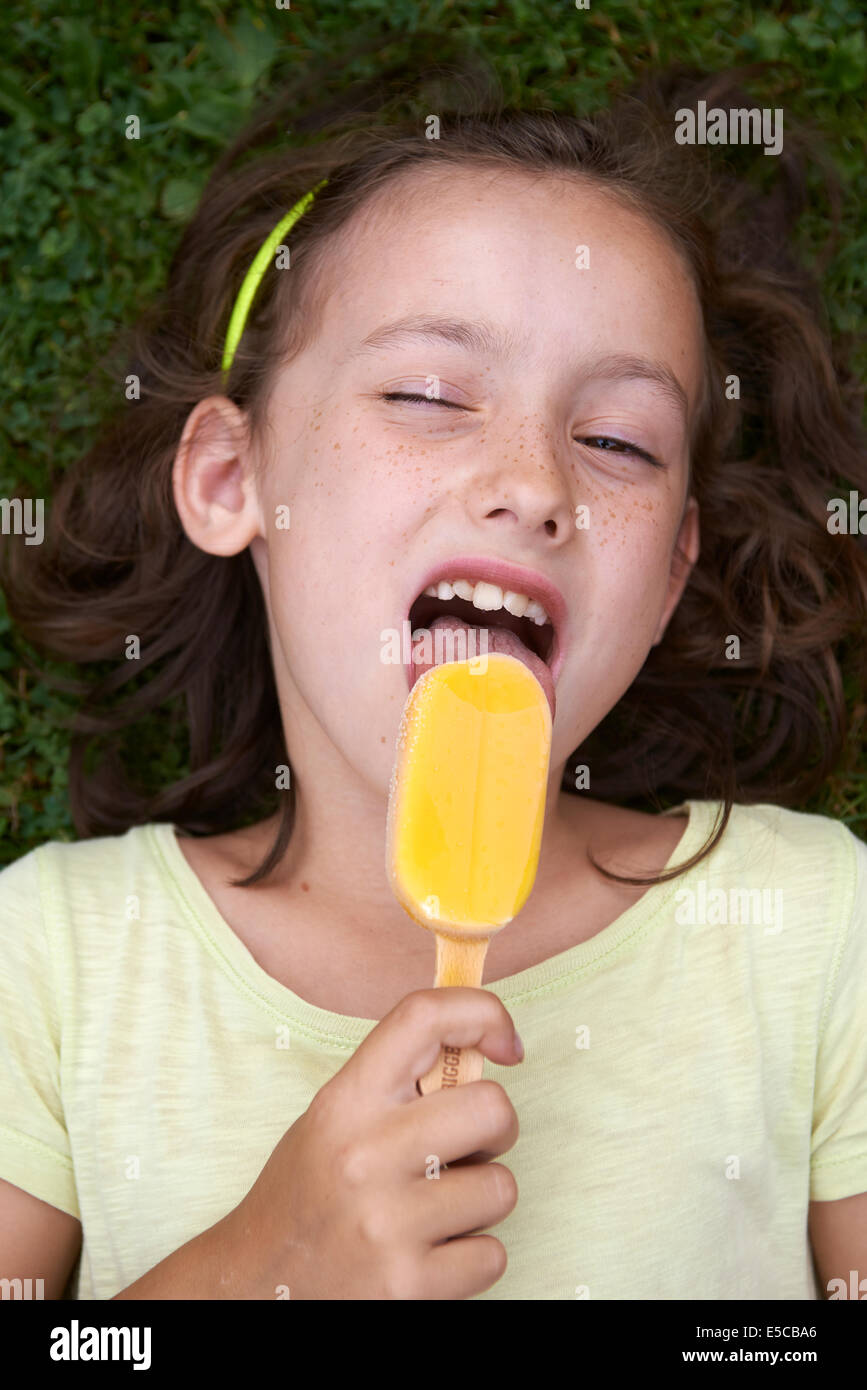 Enfant fille brune foncé léchant une glace, portrait, fond d'herbe à gazon vert couché Banque D'Images