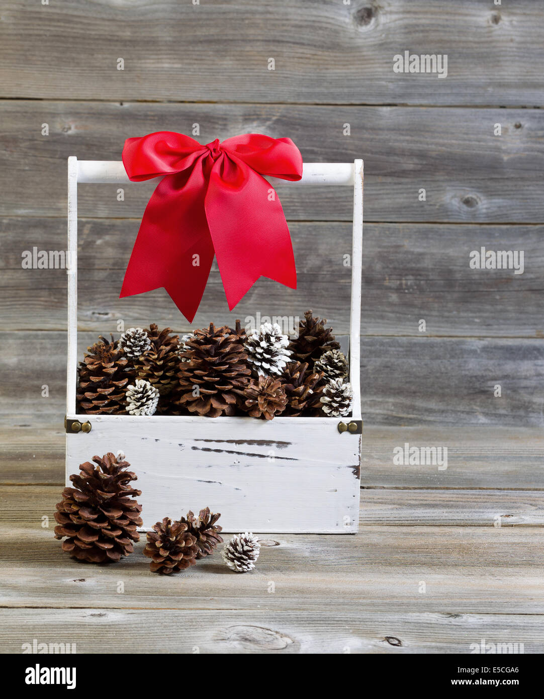 Vue frontale d'une verticale du support en bois rempli de pommes de pin et grand arc rouge pour Noël sur bois rustique Banque D'Images