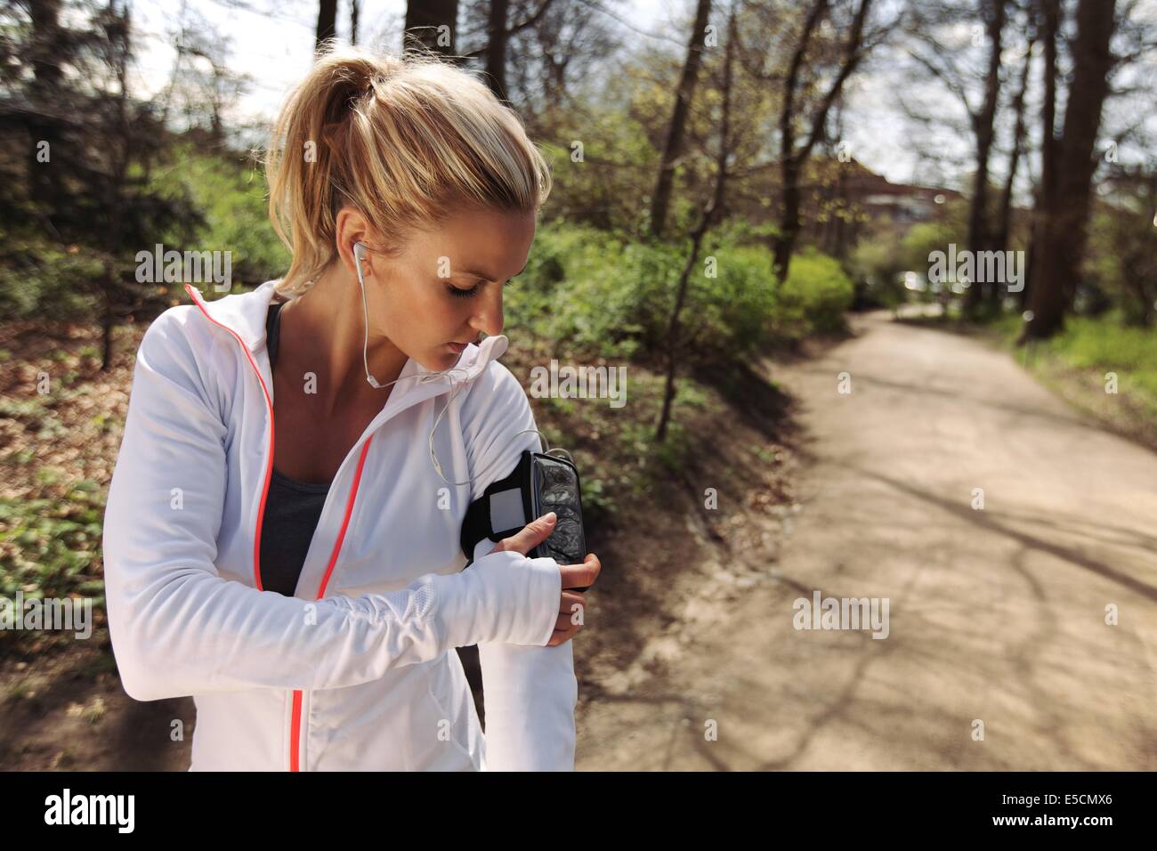 Belle jeune femme de la formation à l'extérieur pendant qu'à l'aide d'un smartphone pour surveiller ses progrès. Caucasian female runner en forêt. Banque D'Images