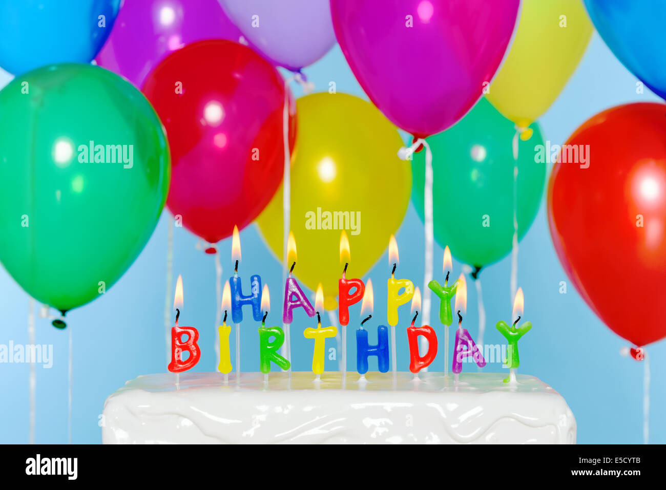 Joyeux anniversaire lettres bougie sur un gâteau avec des ballons colorés en arrière-plan. Banque D'Images